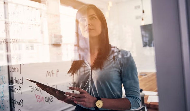A woman writing and planning ideas on a glass whiteboard in an office.